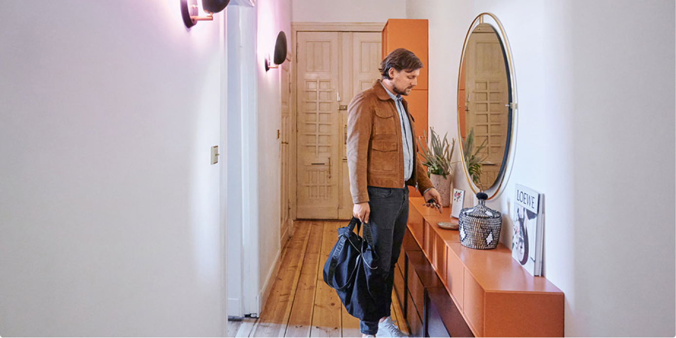 Mann steht im Wohnungsflur mit Tasche in Hand und legt Schlüssel auf Side Board.