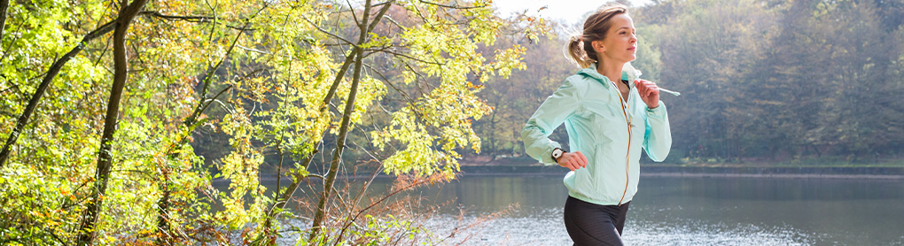 Frau mit Smartwatch joggt um einen See