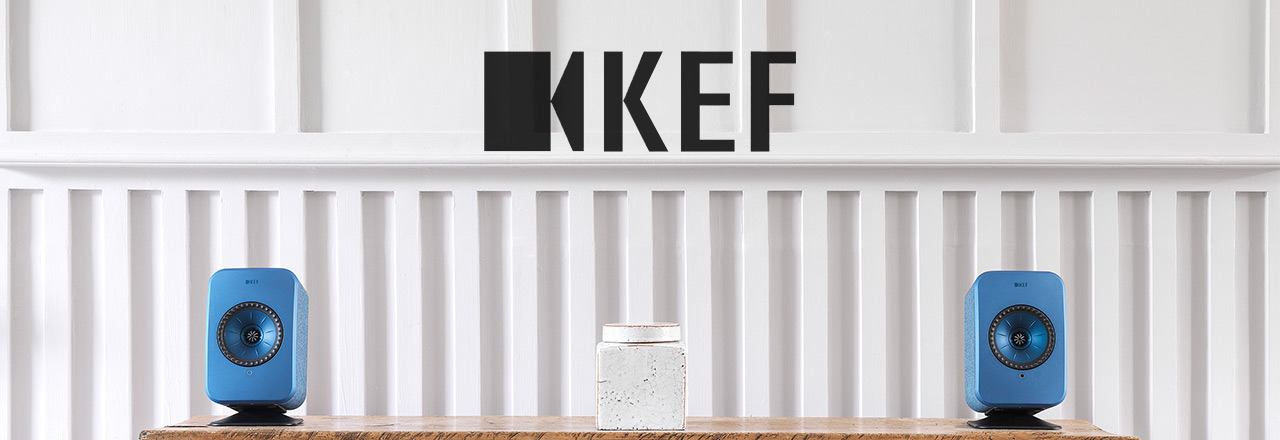  Ein blaues Paar KEF LSX Speaker auf dem Tisch, dazwischen eine weiße Aufbewahrung und drüberschwebend das KEF Logo in schwarz.