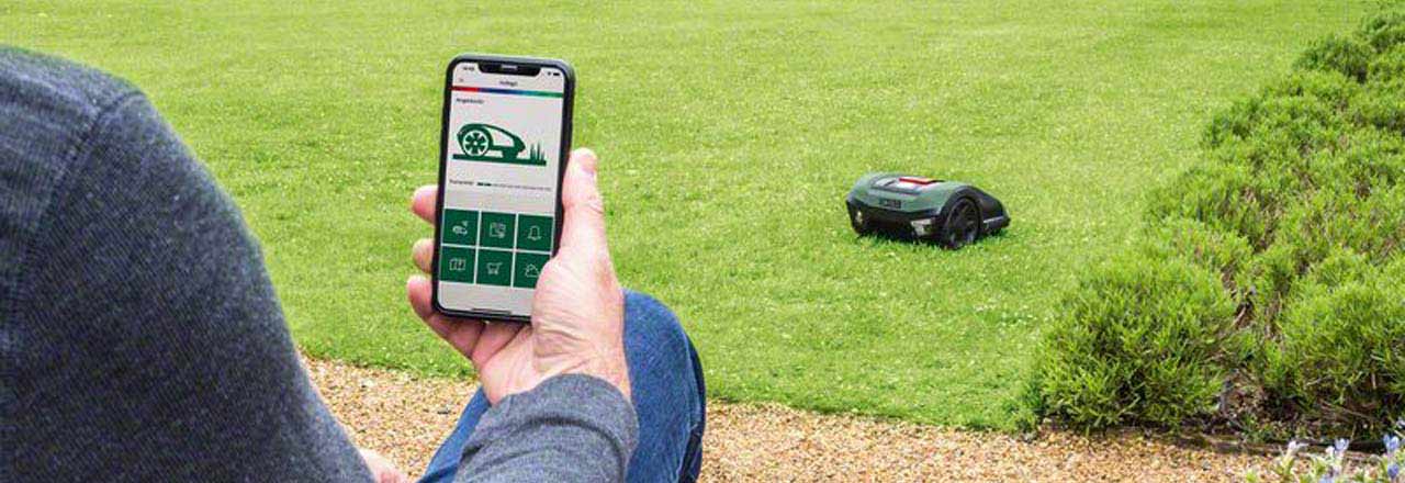 Mann in Garten mit Bosch Mähroboter und Bosch Smartphone App