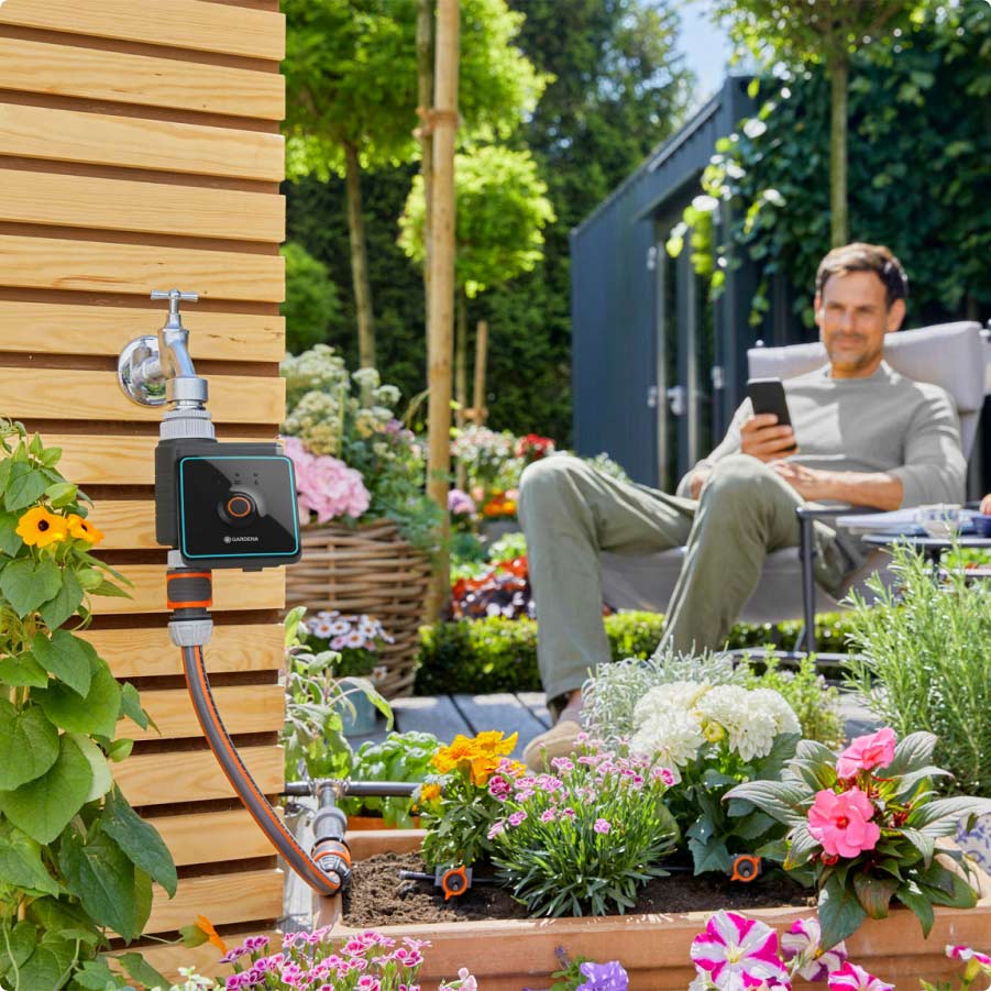 Mann sitzt im Garten neben GARDENA smart system Wassersteuerung
