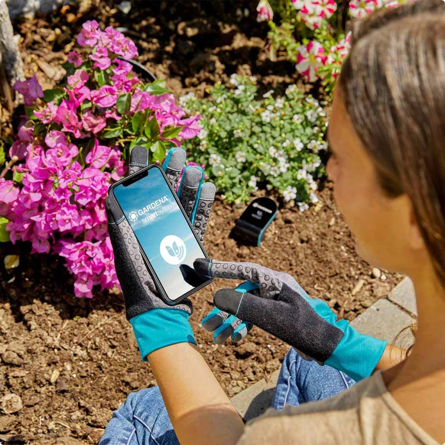 Frau mit GARDENA smart system Smartphone-App an Blumenbeet